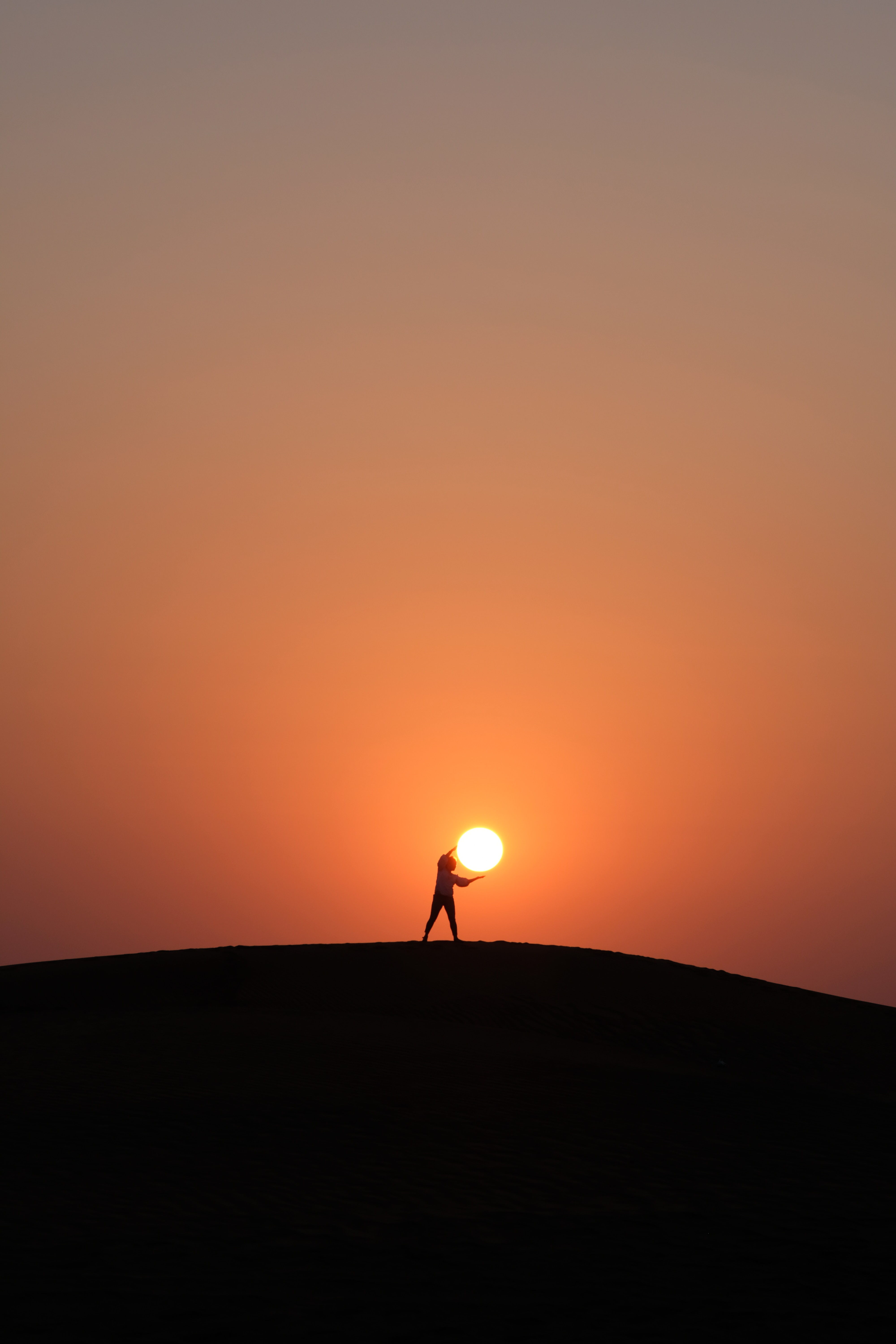 Image of the silhouette of a person appearing to hold the sun on the horizon.